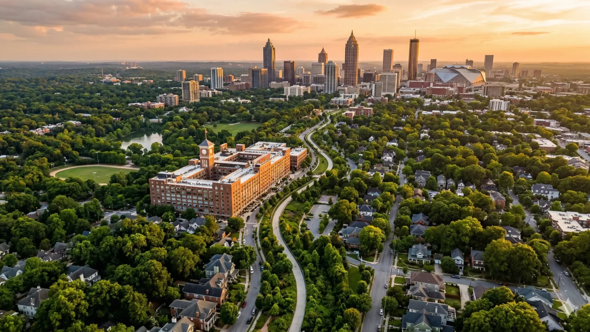 An aerial view of a leafy neighbourhood with a large brick campus and the skyline at sunset