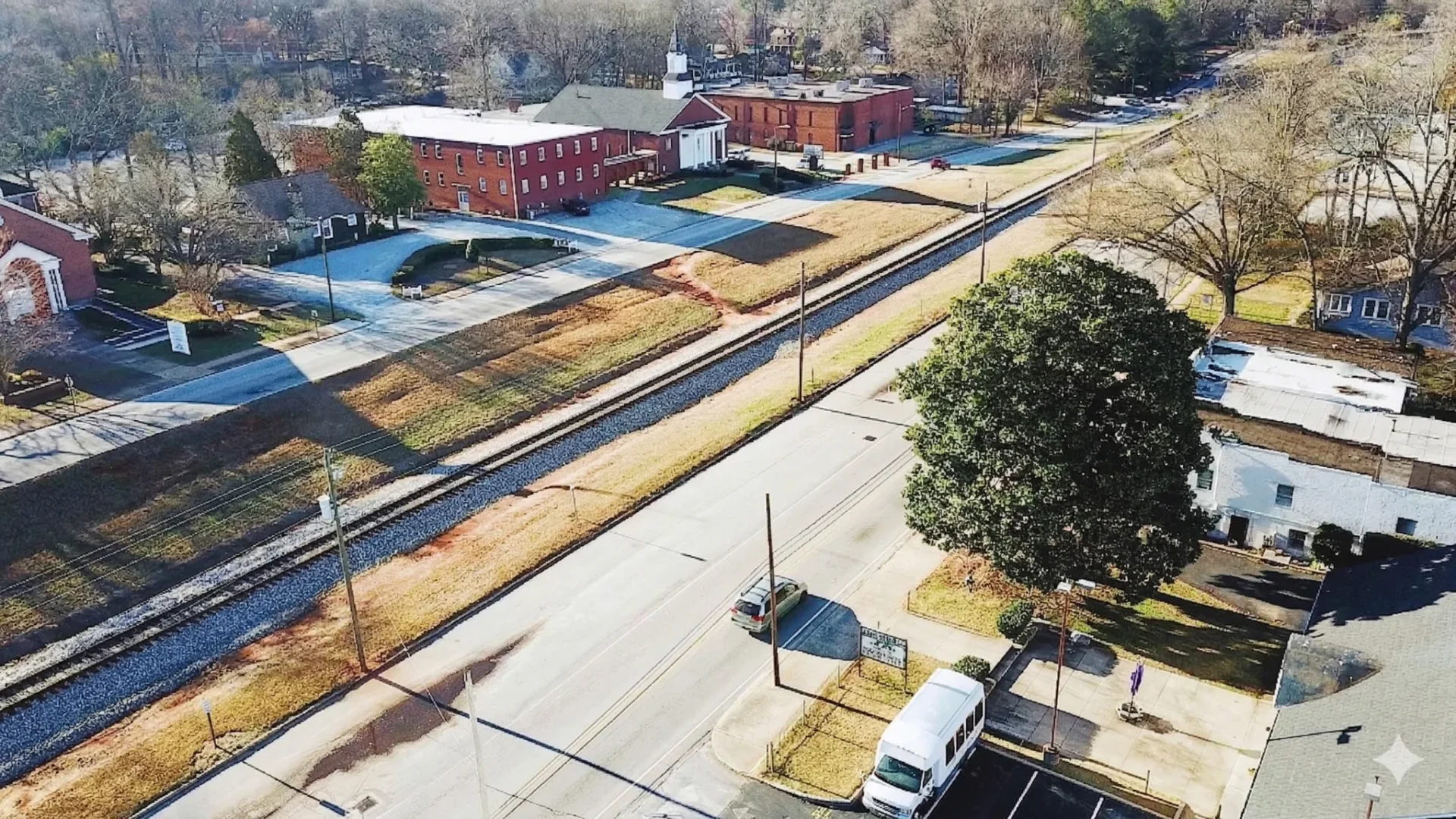 An aerial view of a wide road with a brick building and a rail corridor running alongside