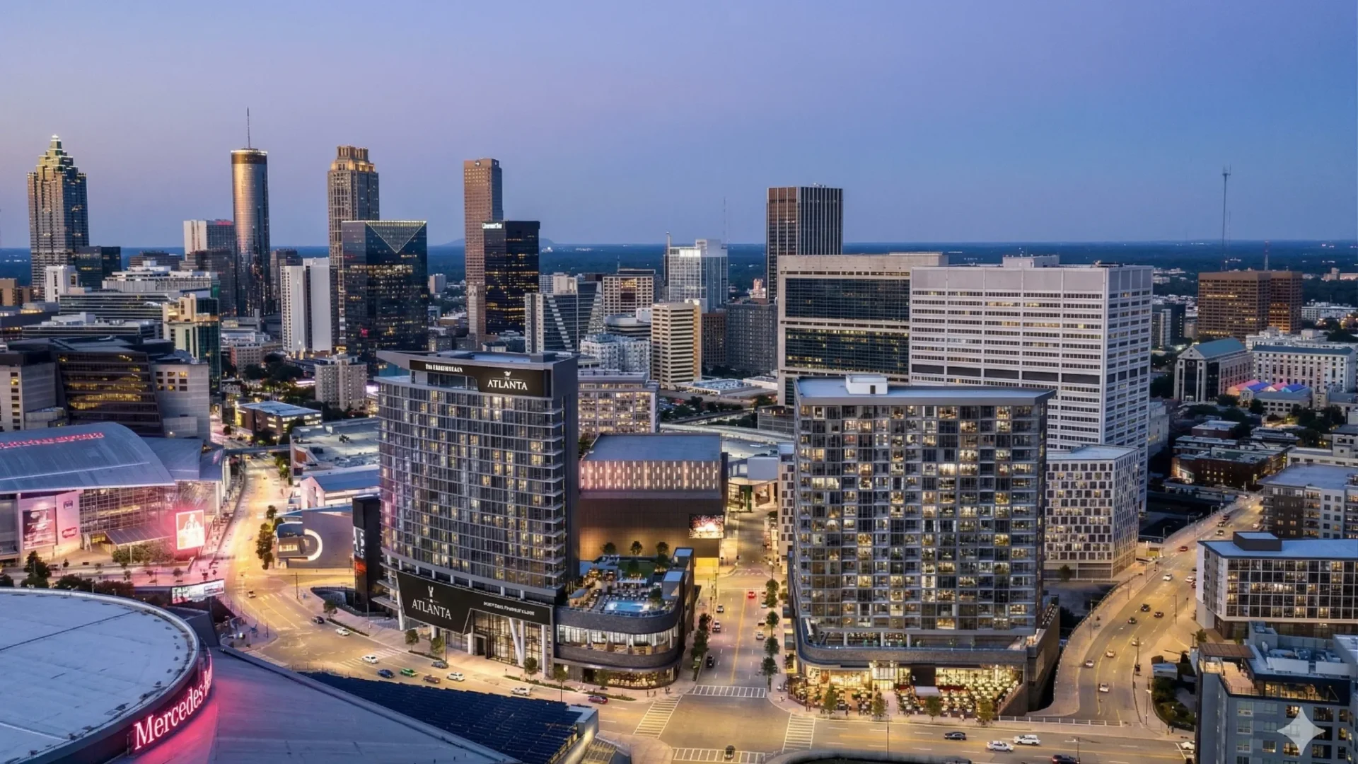 An aerial view of a lit stadium district at dusk with the skyline behind