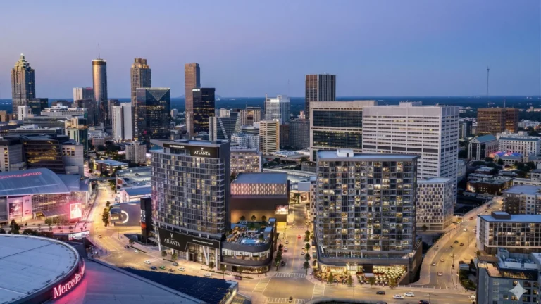 An aerial view of a lit stadium district at dusk with the skyline behind