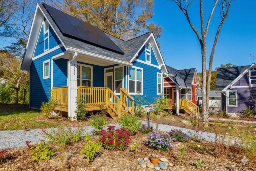 A blue bungalow with a yellow painted porch behind a bed of wildflowers