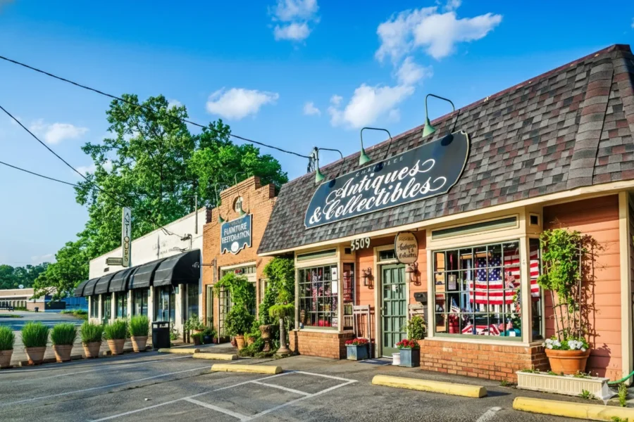 A row of brick shopfronts with awnings and planters along a small parking lot
