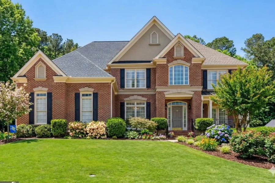 A brick and stucco two-storey house with black shutters above a sloping lawn