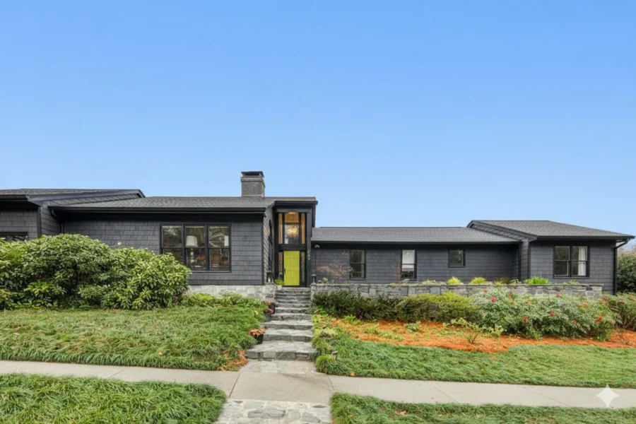 A dark painted ranch house with a yellow front door and a stepped walk