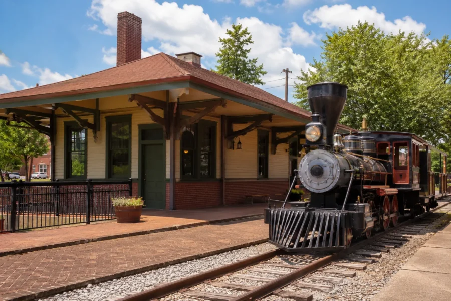 A restored railroad depot with a black steam locomotive standing on the tracks beside it
