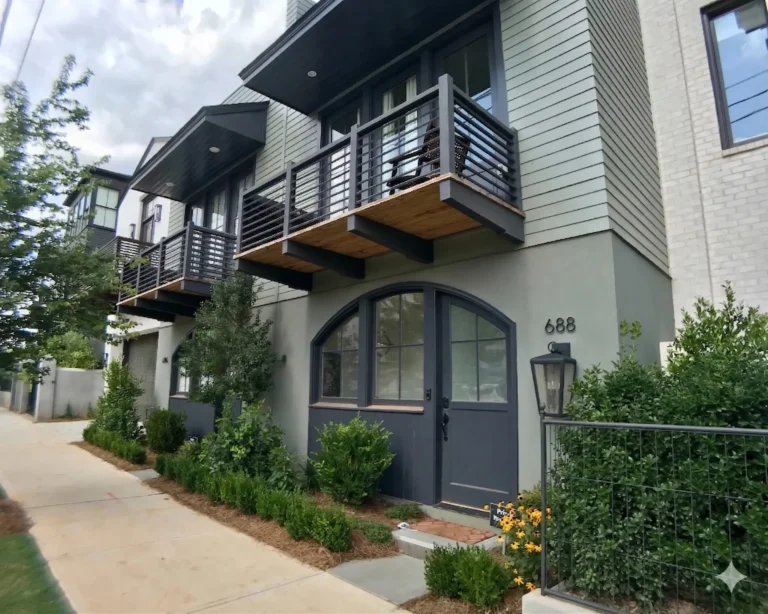 A modern grey townhome with an arched front door and a balcony above the entry