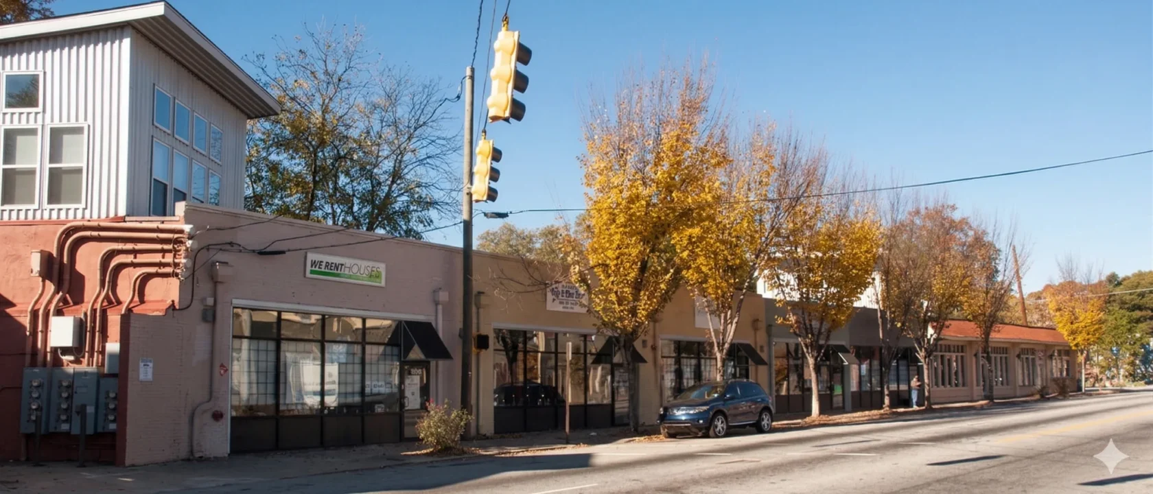 A row of low commercial buildings along a street lined with autumn trees
