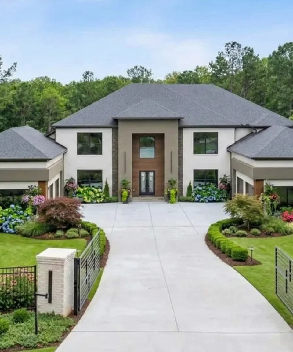 A modern stucco house at the end of a gated drive between planted beds