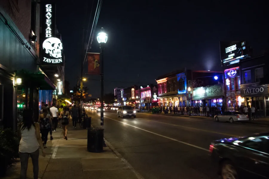 A neon-lit commercial strip at night with bars, shops and passing traffic