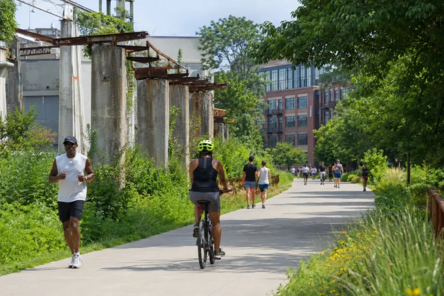 People running and cycling on a paved trail beside a converted industrial structure