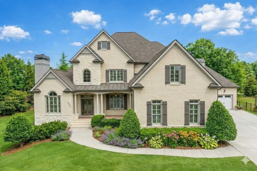 A stone house with an arched entry, shutters and a clipped front hedge