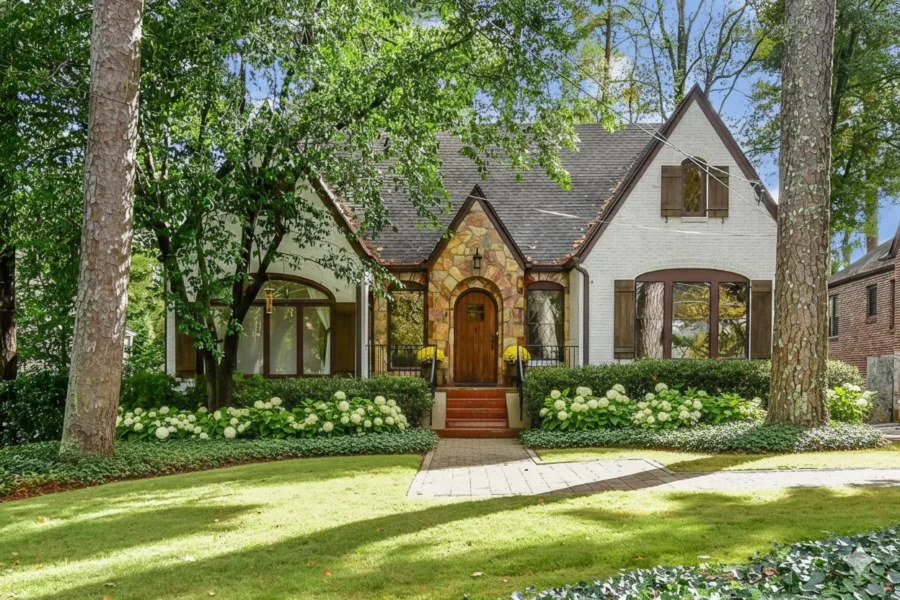 A stone Tudor cottage with an arched front door under tall trees