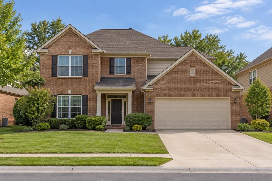 A two storey brick suburban family house with a two car garage, a landscaped front lawn and a concrete driveway