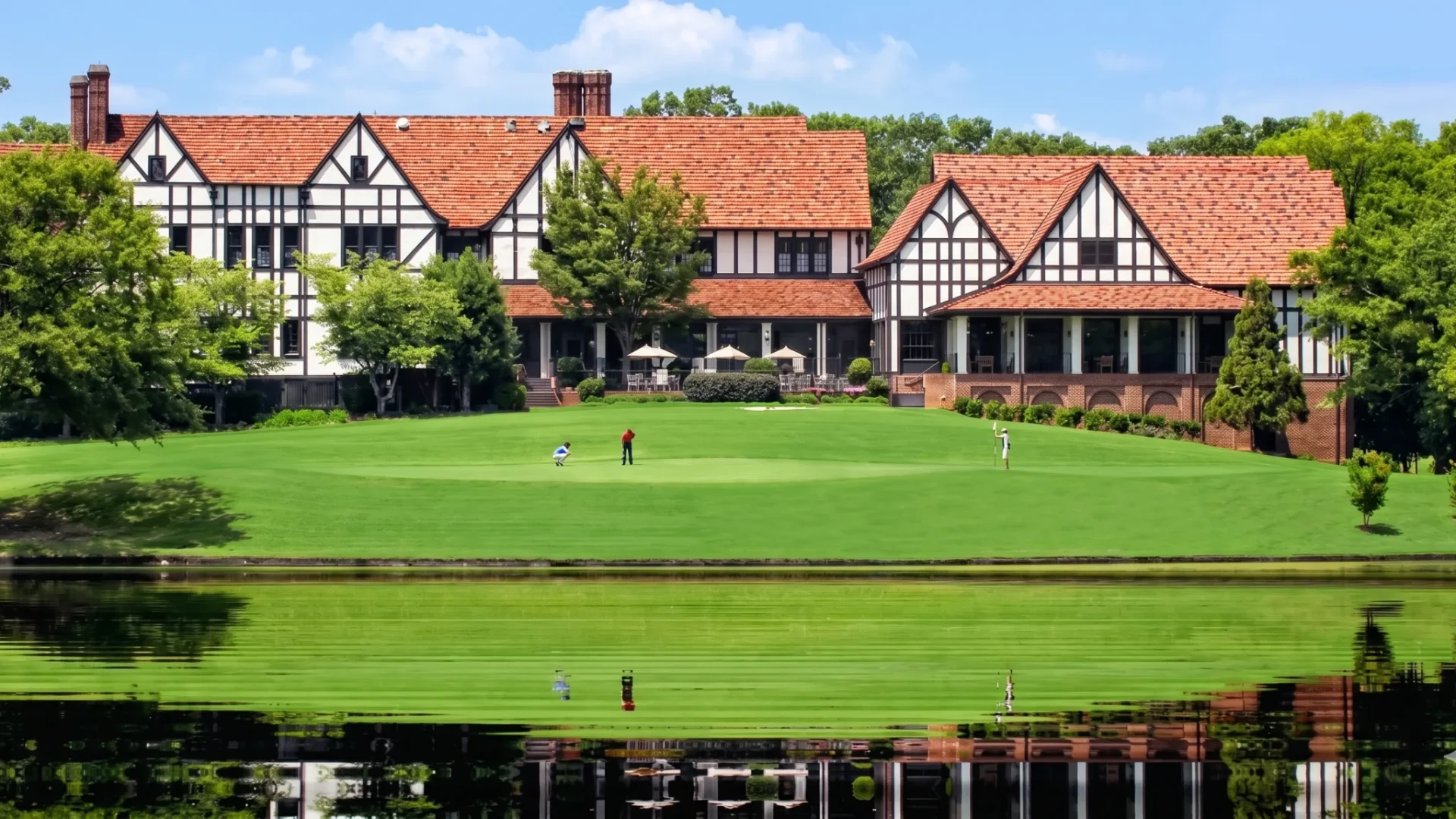 A large Tudor clubhouse across a manicured lawn and a still lake
