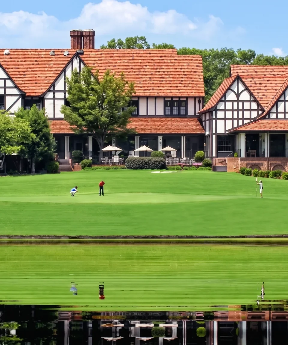 A large Tudor clubhouse across a manicured lawn and a still lake
