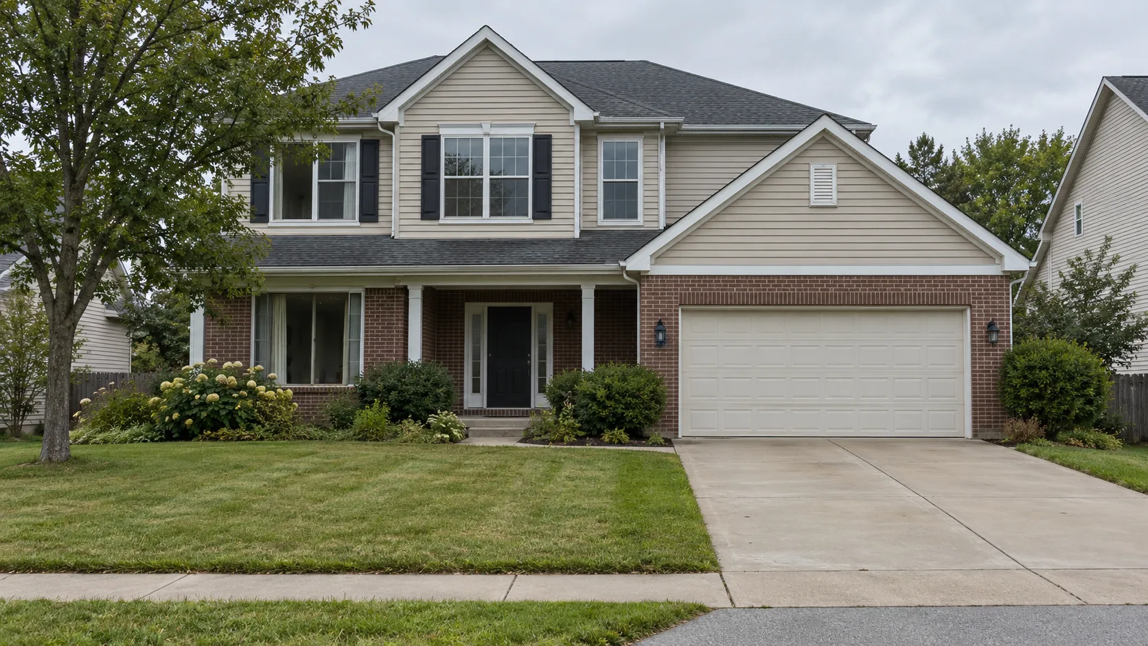 An ordinary suburban two storey house in brick and siding seen from the street on an overcast day, with an empty driveway and a recently cut lawn