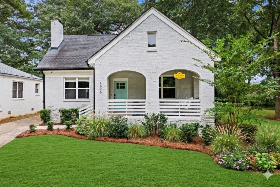 A white painted brick cottage with arched windows and a low porch rail above a lawn