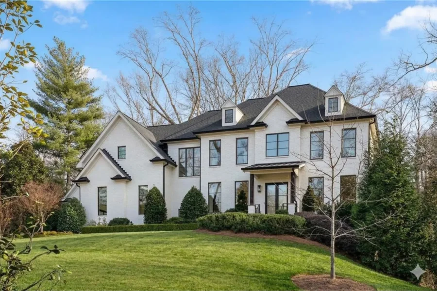 A white painted brick house with dark window trim on a gently sloping lawn
