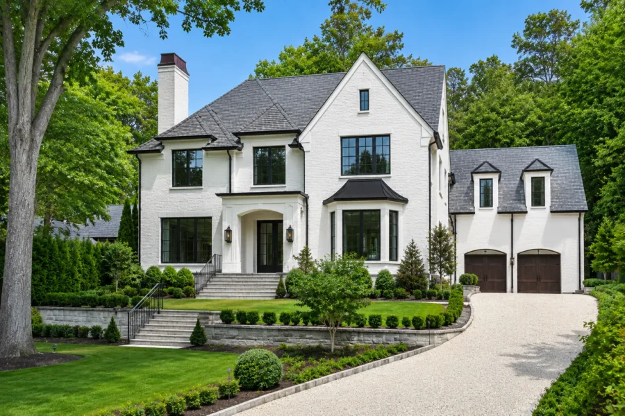 A large white brick house with a steep dark roof, a two car garage and a curving gravel driveway