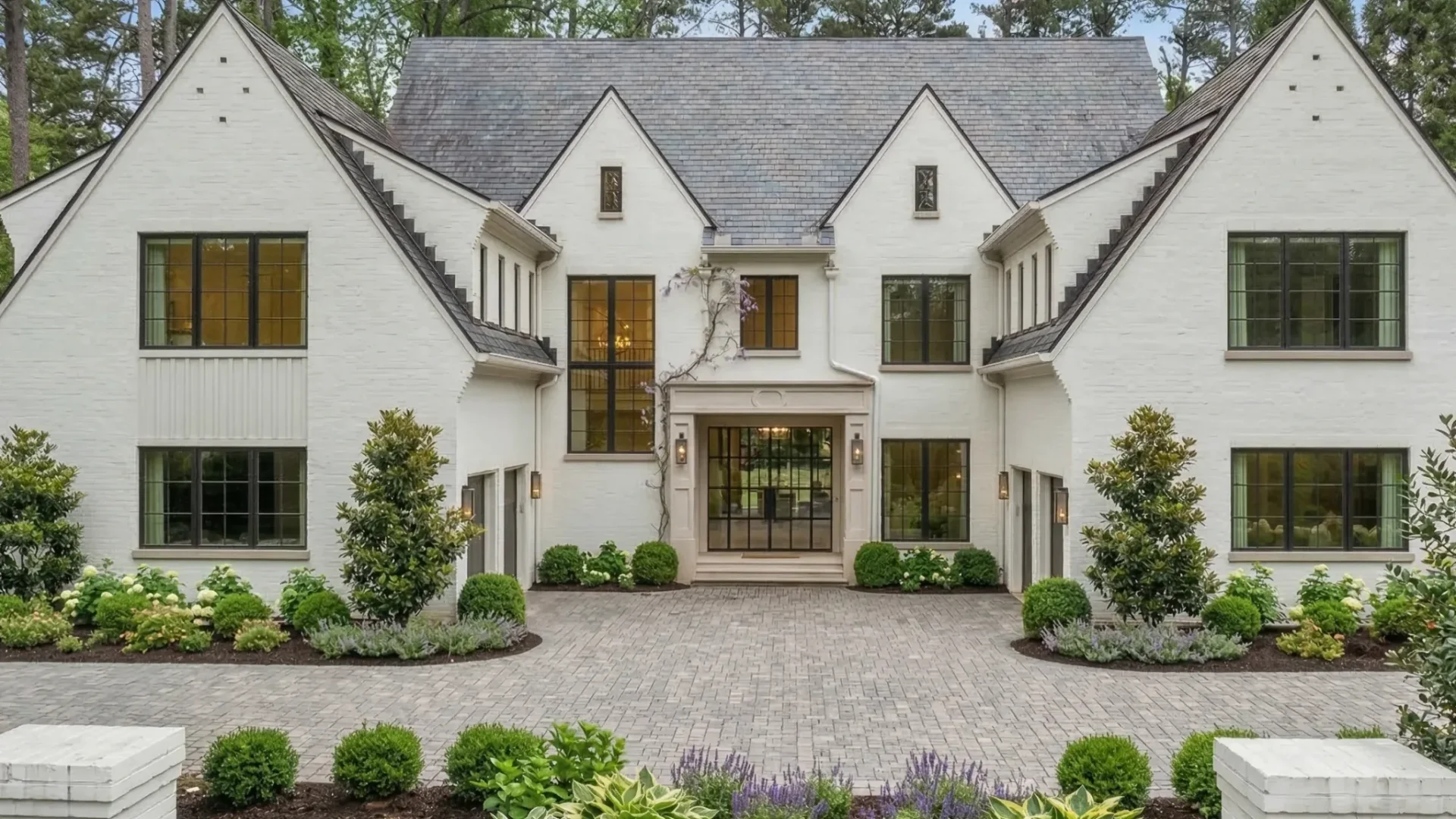 A white painted brick house with steep gables and a paved forecourt