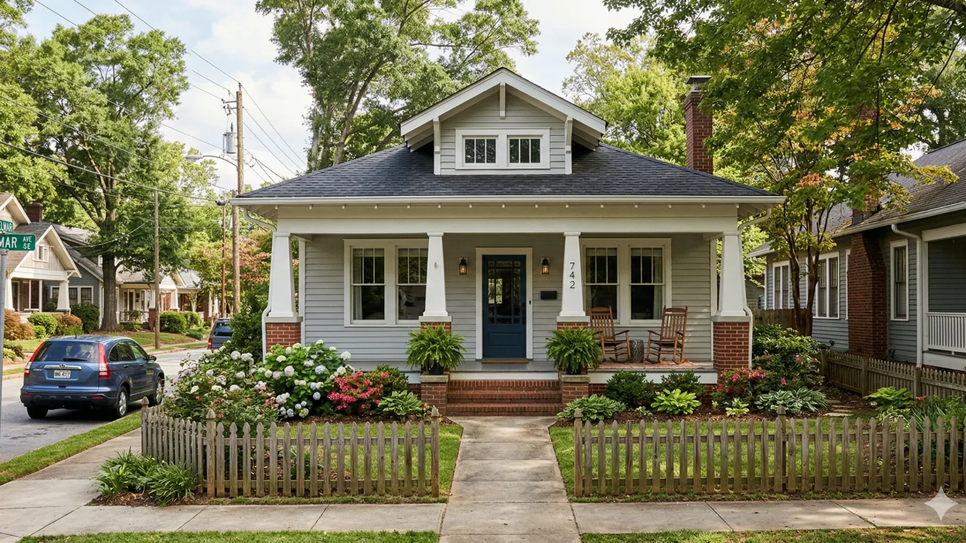 A white bungalow with a deep porch behind a low picket fence