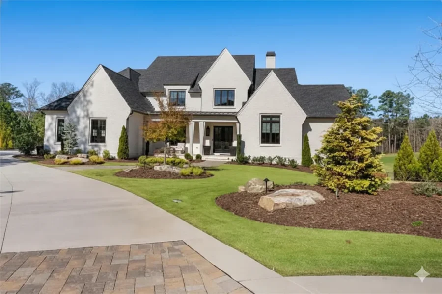 A white modern farmhouse with black windows, a wide driveway and manicured landscaping