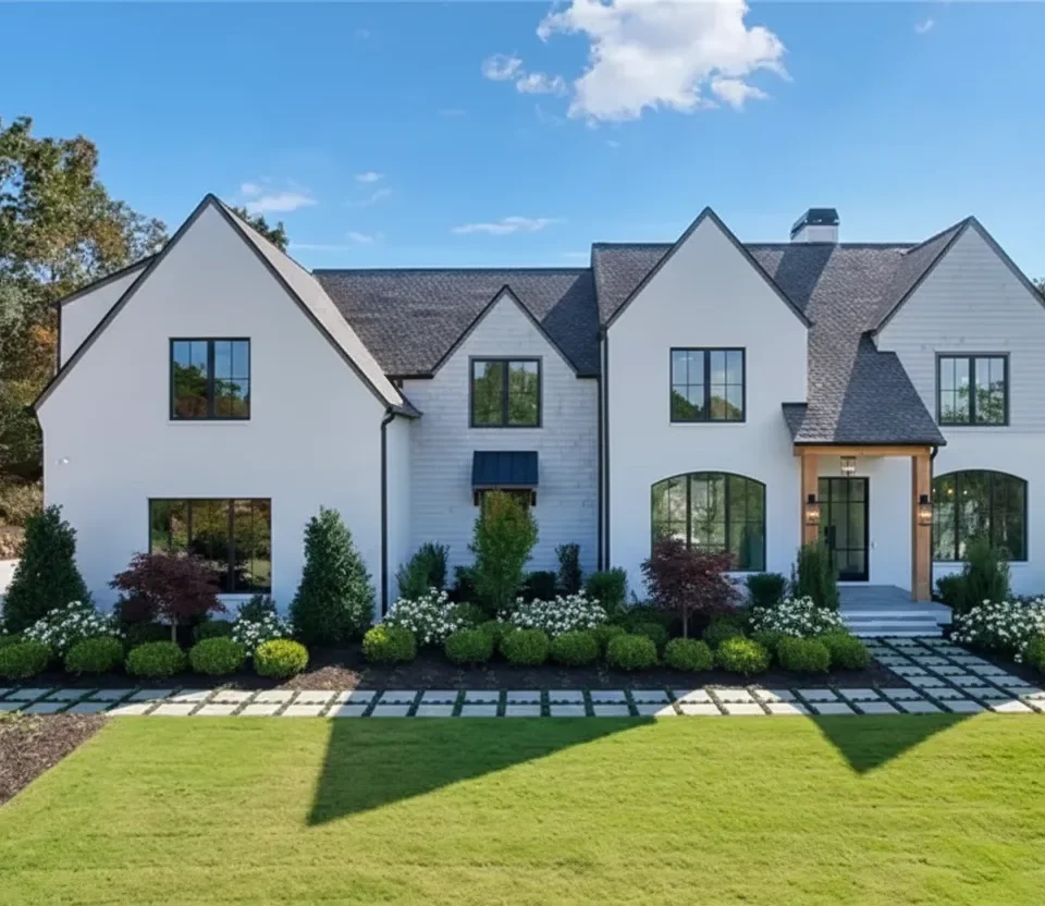 A white modern house with dark window trim behind clipped hedges