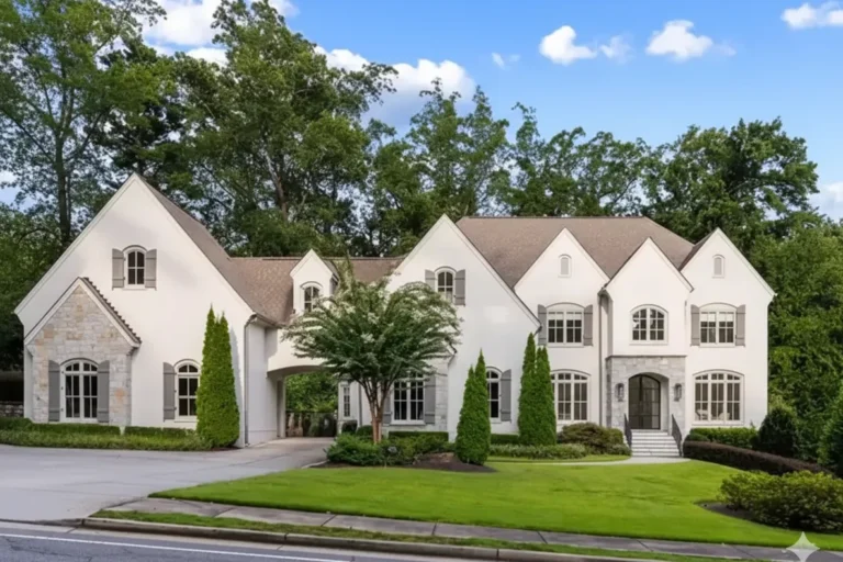 A large white stone and stucco house with steep gables and a manicured lawn